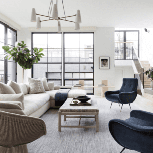 living room with vintage furniture, tan couch and navy blue chairs, white walls, large windows and modern chandalier