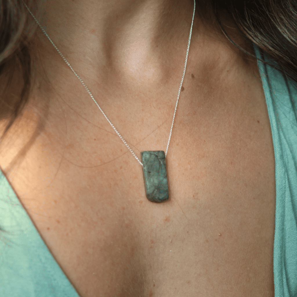 rectangle stone necklace on silver chain shown on a women's neck with a green v neck shirt