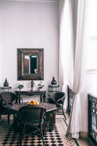 Room with white walls and vintage black wicker chairs, mirror and black checkered floors