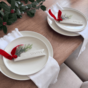 Christmas place setting with white plates and napkin and red ribbon and pine name tag