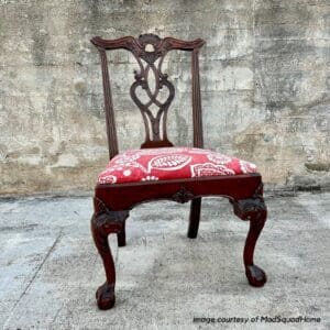 traditional wood chippendale style chair with red floral upholstered seat sitting on concrete with concrete wall in background