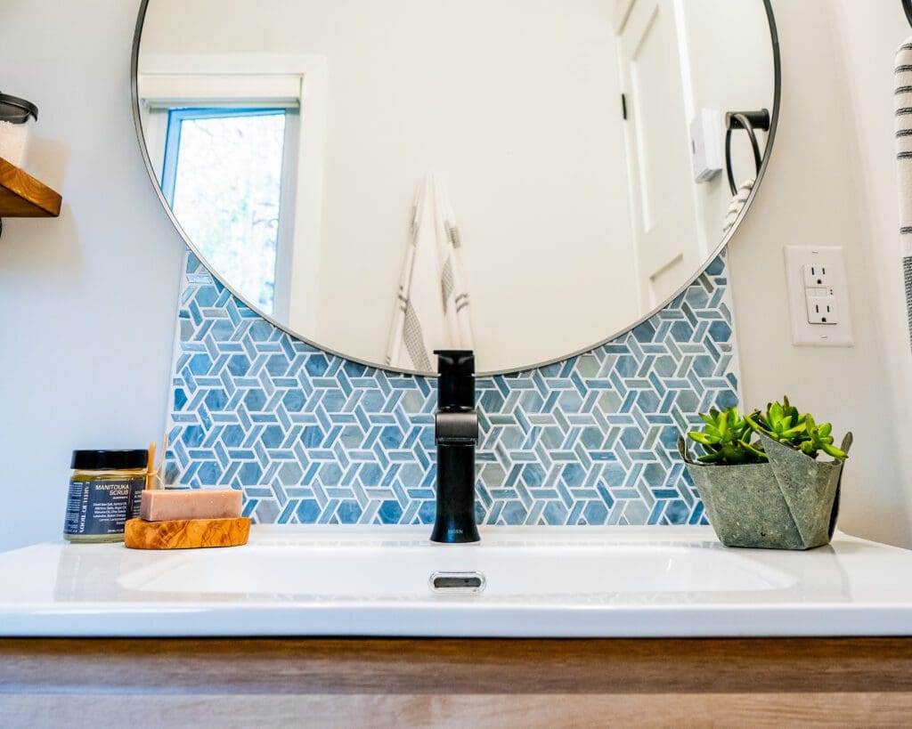 Detail of a powder room including a round mirror, blue tile, sink countertop and plant