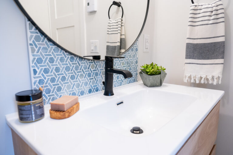 sustainable bathroom renovation with round mirror, white sink and blue tile backsplash