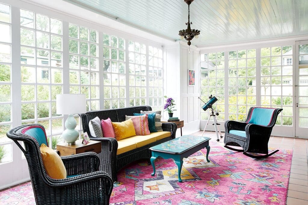 finished sunroom renovation with black wicker furniture and bright pink rug